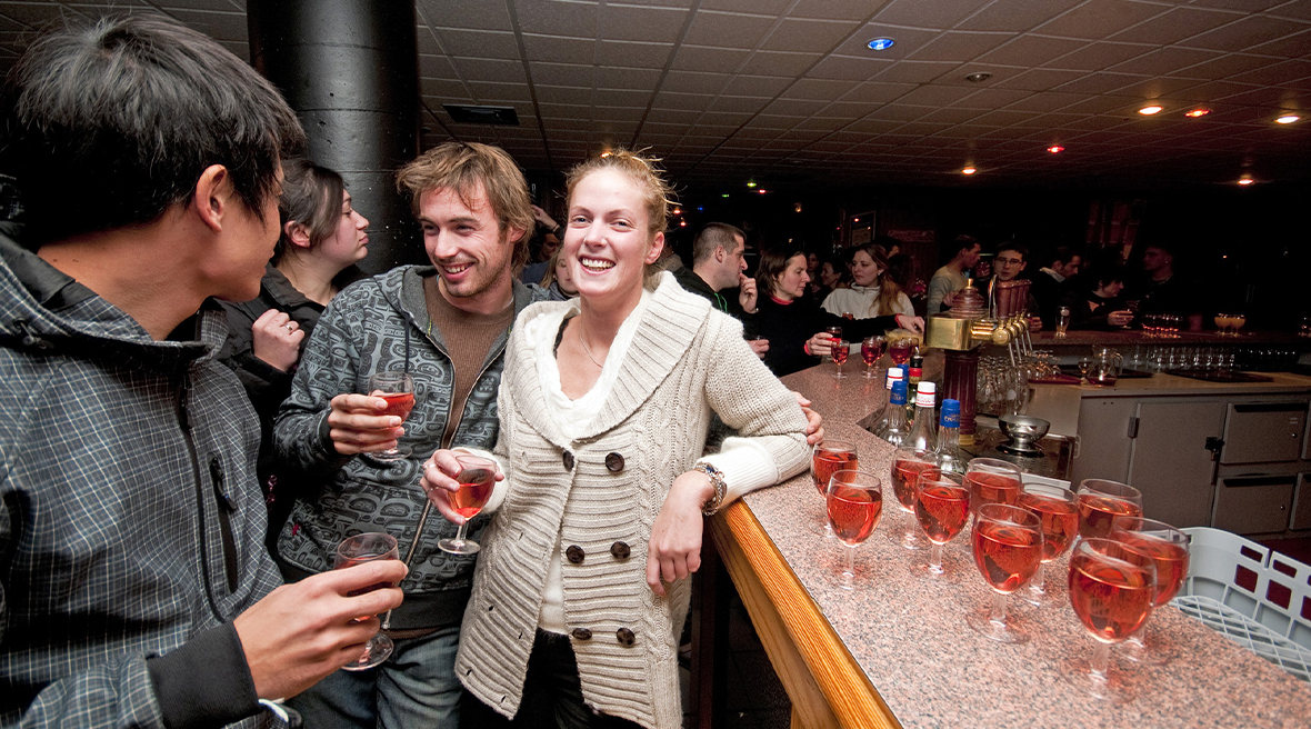 A couple in the foreground laughing and enjoying apres ski drinks in a busy bar environment